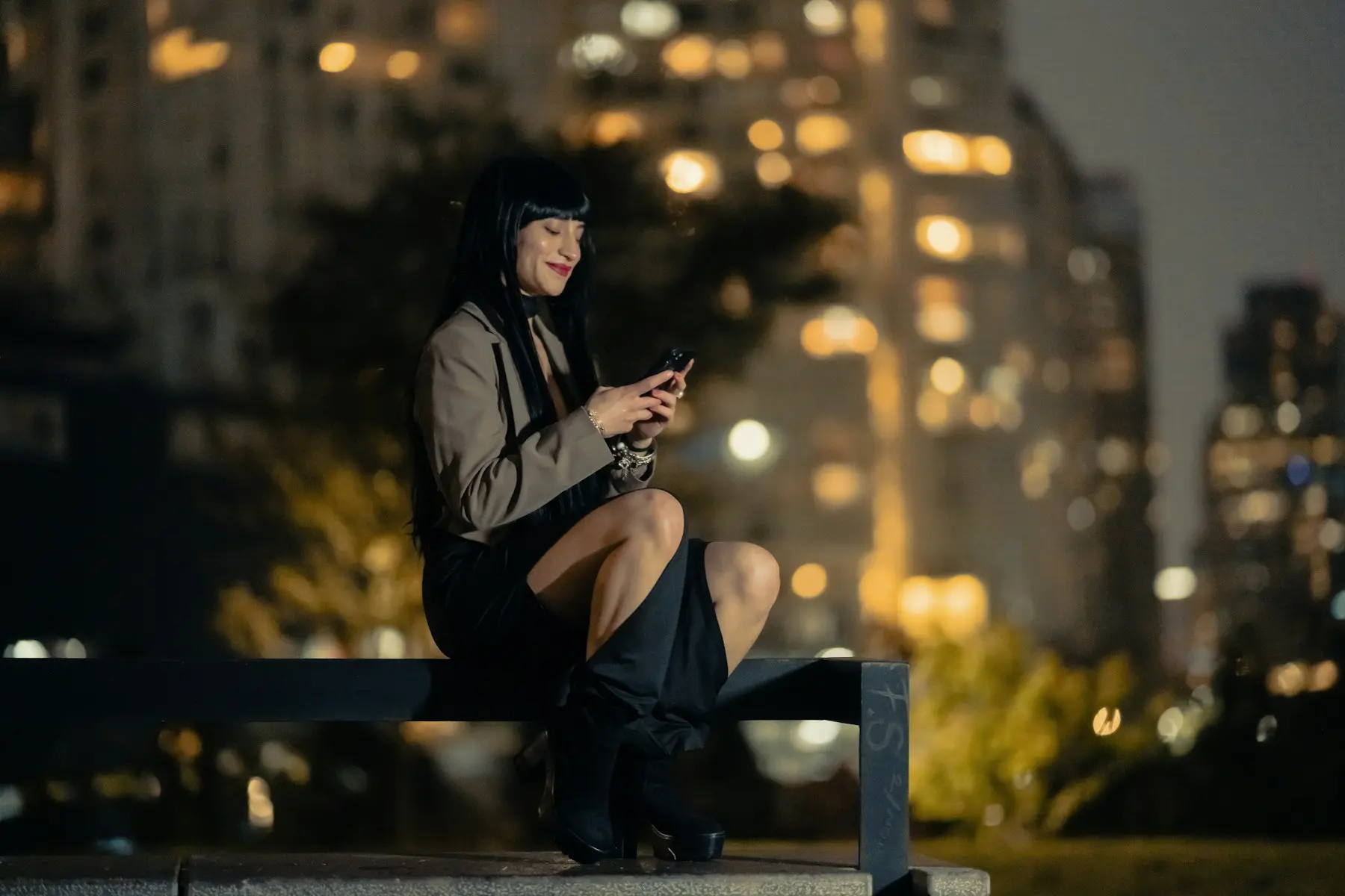 Una mujer sonríe mientras escribe en su celular en un parque de la ciudad, de noche