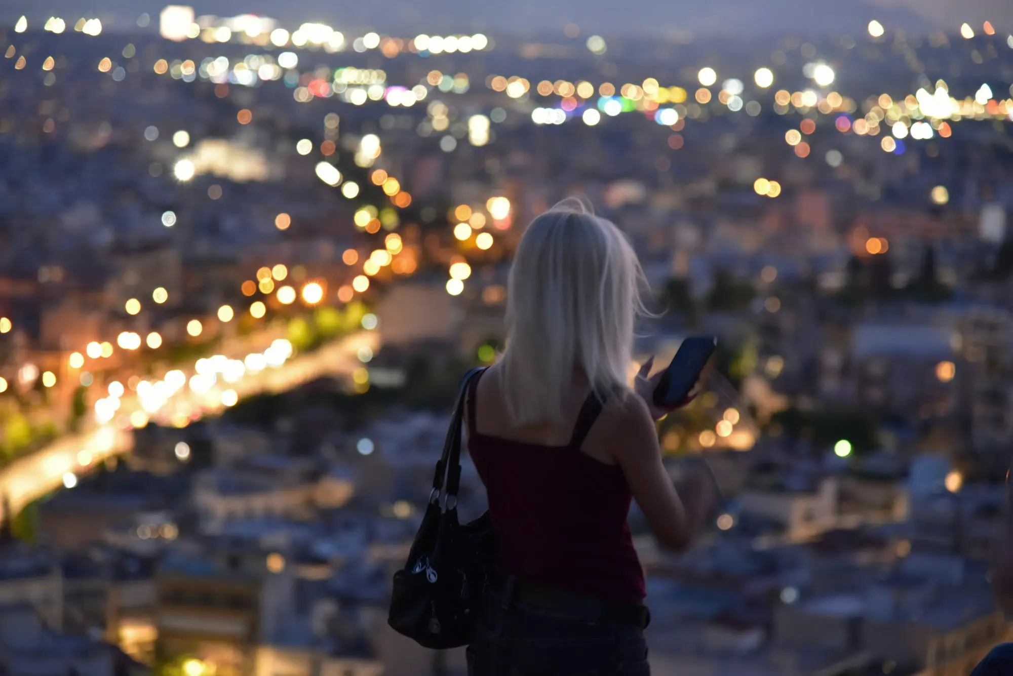 Una mujer revisa su celular frente a la ciudad iluminada al anochecer
