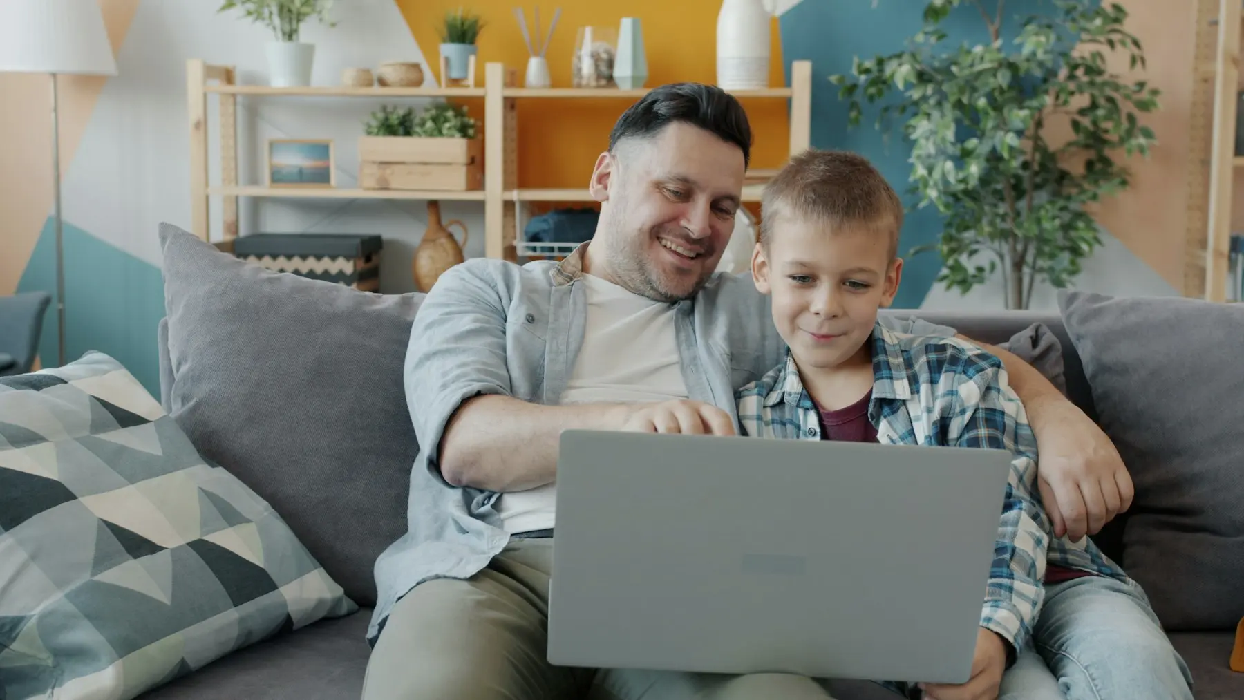 Un papá y su hijo ven algo en la laptop en la sala de su casa