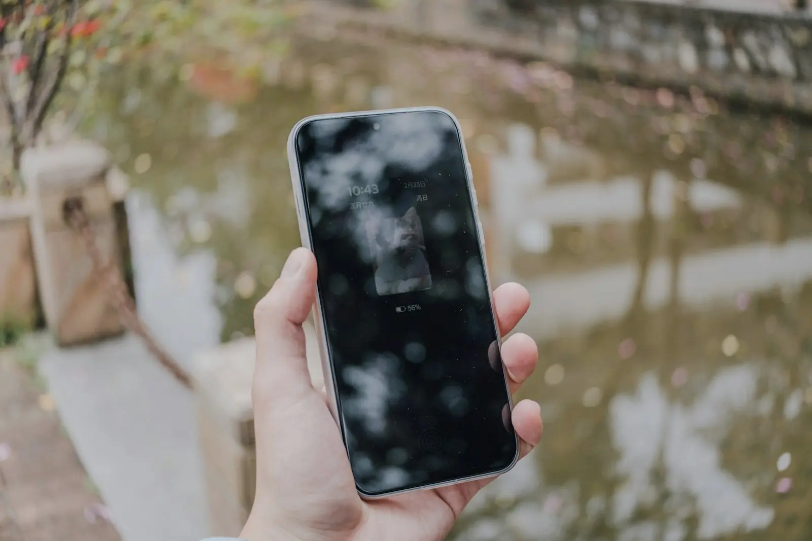 Una mano sostiene un celular junto a un canal, con la pantalla bloqueada
